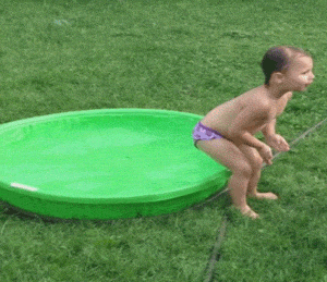 Video gif. In a clip from AFV, a child in a bathing suit prepares to drop into a seated position onto the side of a full plastic kiddie pool, ostensibly tipping it over...but instead they just land on the ground. The child looks at us with surprise.