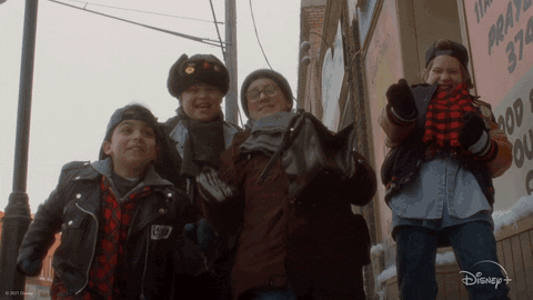 Disney gif. Four boys in The Mighty Ducks: Game Changers give each other five and celebrate as they stand together in winter gear on a city street.