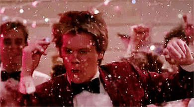 Movie gif. A party rages and confetti falls as Kevin Bacon as Ren in Footloose twirls, then shrugs confidently and straightens his bowtie. The crowd around him applauds.