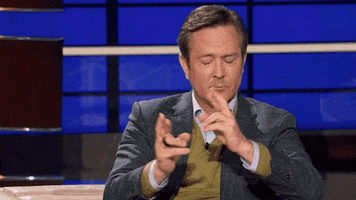 TV gif. A scene from To Tell the Truth. Wearing a dark plaid blazer, Thomas Lennon hopes for a good outcome as he closes his eyes and crosses his fingers.