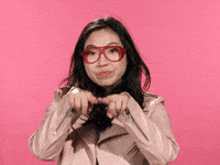 Celebrity gif. Awkwafina smiles as she draws a green heart in the air with her fingers, then pokes it, and it bursts.