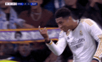 Sports gif. Jude Bellingham of Real Madrid walks across the field with a big smile on his face gesturing with his finger like he wants you to come closer. 