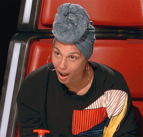 TV gif. Wearing a grayish-blue head wrap and large hoop earrings, Alicia Keys from The Voice gives us a stunned, smiling, slack-jawed blink.