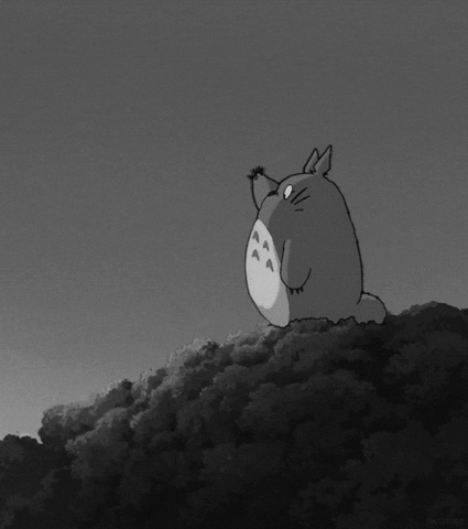 Anime gif. Totoro from My Neighbor Totoro stands on top of a hill, looking down and waving.