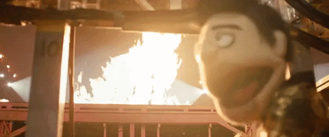 Music Video gif. The puppet from Panic! At The Disco's video for Dancing’s Not a Crime has set something on fire and it looks pleased as it laughs.