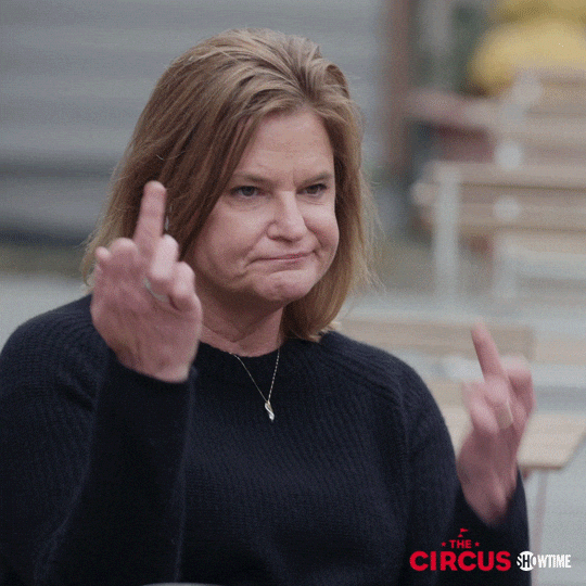 TV gif. Jennifer Palmieri in The Circus frowns as she brandishes a middle finger on each hand.
