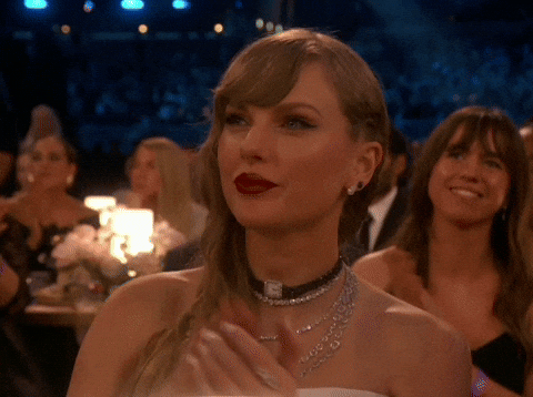 Celebrity gif. Taylor Swift sits in the audience at the Grammys. She nods and claps her hands together.