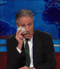Daily Show gif. Pretending to cry, Jon Stewart wipes his tears with a hundred-dollar bill.