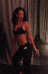 Celebrity gif. Rihanna wears a black bikini top and a pair of black sweats as she twerks and tosses her head seductively.