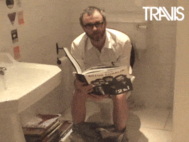 Video gif. Zoom on Fran Healy of Travis, sitting on the toilet looking at us, bent over a huge book. 