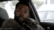 TV gif. A man in the driver's seat of a parked car looks away from us and shakes his head. He looks stunned. Text, "Damn."