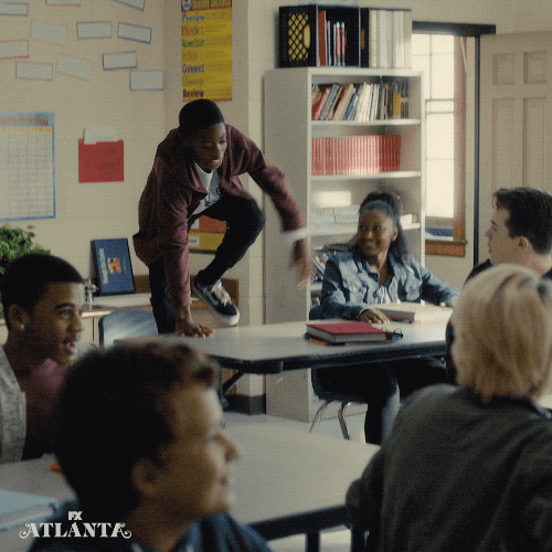 TV gif. On Atlanta, young kid in a classroom stands up on his desk and dances, while his classmates cheer him on.