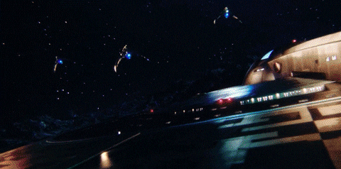 TV gif. Three Klingon warships in Star Trek Discovery attack a Federation starship, two dropping green bombs which explode in an orange fireball against the starship’s shields.