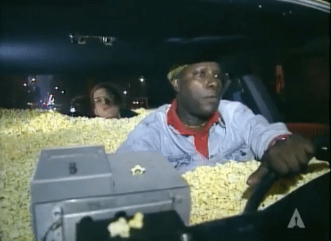 Celebrity gif. From the 1995 Academy Awards, a dash-cam view of a taxi driver whose car is full of popcorn, driving David Letterman in the backseat, as they both take nibbles of popcorn.