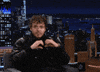 Celebrity gif. Jack Harlow on The Tonight Show Starring Jimmy Fallon makes a heart with his hands at the audience. 