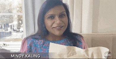 TV gif. A Mindy Kaling from the 2020 Emmys is seated on a couch, a sewing needle in one hand and a needlepoint frame in the other. We tilt down to see the writing on the needlepoint. Text, "Help I'm going insane."