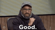 SNL gif. Chris Redd with a bushy, graying beard, dressed in a hoodie, glasses, and a baseball hat looks at someone with piqued interest. He nods his head slowly and says, “good.”