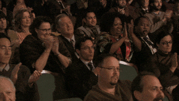 The Office gif. Phyllis, Bob Vance, and other people in the audience get up from their seats to give a standing ovation, while Leslie David Baker as Stanley looks at us begrudgingly and rises.