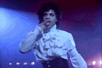 Celebrity gif. Prince dances onstage, licking his finger and then smoothing back his curly hair.