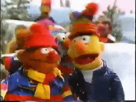 Muppets gif. Bundled up, Bert and Ernie sing Christmas carols with a crowd of Muppets as the snow falls around them in A Muppet Family Christmas.