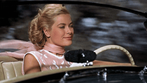 Movie gif. Grace Kelly as Frances Stevens in To Catch a Thief drives in a convertible car. Her hair and scarf blow in the wind as she speeds down the road. She has a satisfied smile on her face. 