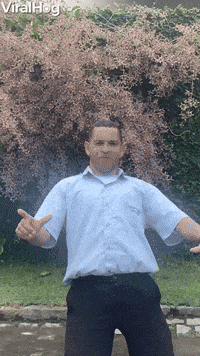 Video gif. Man poses awkwardly as we zoom out away from him. As he poses, almost frozen like a statue, a white dog jumps up and bites his crotch The man quickly grabs his groin in pain as the dog walks through his legs.