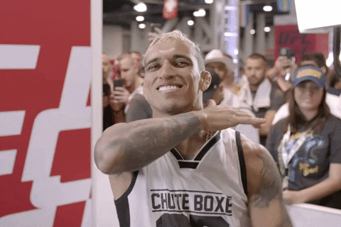 Sports gif. UFC fighter Charles Oliveira looks at us with a big smile. He moves his hand under his chin.