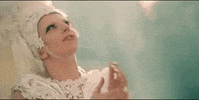 Music video gif. In the video for G.U.Y., dressed in a white floral headdress and dress, Lady Gaga looks hopefully heavenward and clasps her hands together.