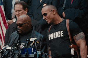 Movie gif. Samuel L Jackson as PK Highsmith and Dwayne The Rock Johnson as Danson, in The Other Guys, at a press gaggle, as The Rock leans into the microphones, smiling and saying "No comment, but yes."