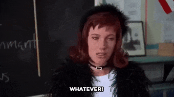 Movie gif. Elisa Donovan as Amber from Clueless wears a black feathered coat and headband with her red hair flipped out at the ends. She gets sassy with her fingers held up in a 'W' as she's saying, "Whatever."