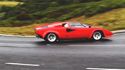 Video gif. A red Lamborghini drives down a winding road. It turns a sharp corner and perfectly drifts then drives on.