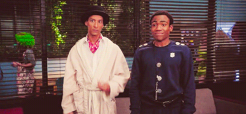 TV gif. Danny Pudi as Abed and Donald Glover as Troy on Community move their arms like waves as they come together and high five. 