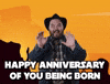 Celebrity gif. Howdy Price, dressed in a plaid flannel, denim jacket, and black cowboy hat, smiles and holds his hands out toward us, saying, "Happy anniversary of you being born," which appears as text.