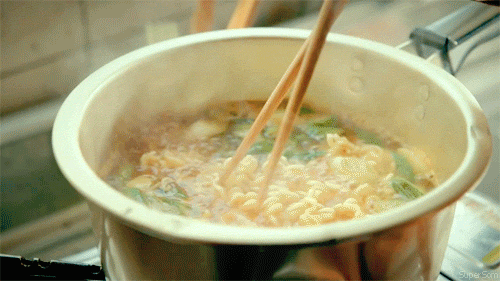 Video gif. Someone uses chopsticks to stir ramen and vegetables cooking in a pot.