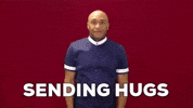 Video gif. A man wraps his arms around himself and hugs himself tight. Text, "Sending hugs."