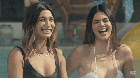 TV gif. Kendall Jenner and Hailey Bieber as themselves, falling into each other in mocking, mean-girl laughter.