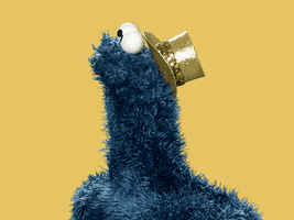 Sesame Street gif. Cookie Monster wears a gold top hat, looking to the side and then turning to us with his mouth open, excited.