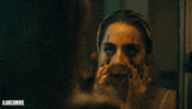 Movie gif. Lady Gaga as Harley Quinn in Joker wears thick black eyeliner as she stares in the mirror, using two fingers to pull at her lower eyelids. 