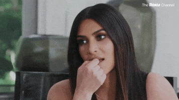 Reality TV gif. Kim Kardashian on Keeping Up With The Kardashians looks at something with a blank stare as she holds her thumbs and index finger in her mouth.