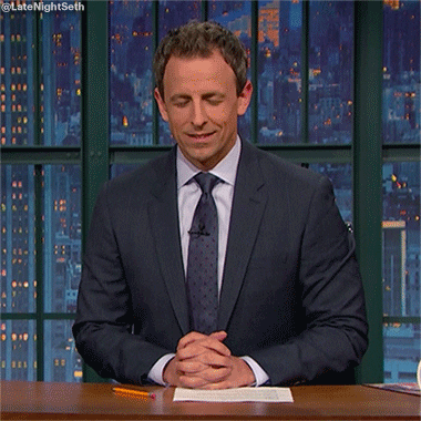 Late Night gif. Seth Meyers sits at his desk with a piece of paper and a pencil in front of him. He has his hands together on top of the desk as he closes his eyes and leans forward, pretending to fall asleep. He then pops up and bats his eyes like he’s been abruptly awakened.