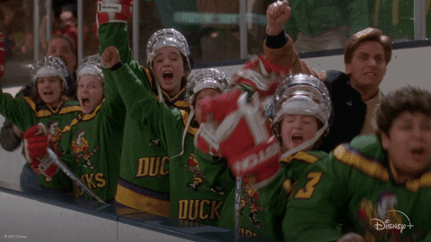 Movie gif. The Mighty Duck hockey team in The Mighty Ducks cheers in excitement in their hockey gear. They hug each other, scream, raise their hands up, and jump up and down in celebration.