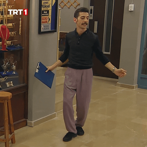 TV gif. Butik Ali does a silly little dance, tapping his feet and holding his arms out, holding a clipboard. At the end of the movement he throws his head back and kicks one foot out. 