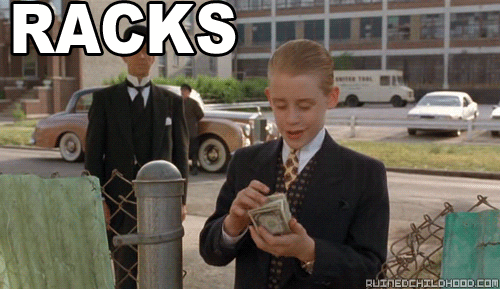 Movie gif. Macaulay Culkin as Richie Rich, hair slicked back and wearing a business suit, fingers through a stack of cash and smiles. Flashing text reads, "Racks on racks on racks."