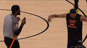 Sports gif. Deandre Jordan dances on a basketball court, hopping up and down, holding his arms up in the air, and twirls. He dances with another man who holds a broom with hops around with him excitedly.