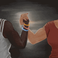 Digital art gif. Two people flex their biceps as they clasp hands in front of a gray-painted background. Text, “Los derechos reproductivos y LGBTQ+ = la lucha por decidir sobre nuestros cuerpos.”