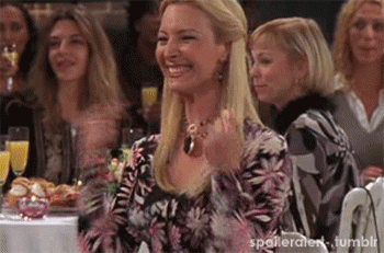 Friends gif. At a banquet, Lisa Kudrow as Phoebe Buffay points to herself excitedly and laughs.