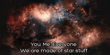 An image of a colorful, bright nebula with various shades of red, orange, blue, and black, representing a cosmic scene with numerous stars scattered throughout. Neil Degrasse Tyson appears in the image, walking forward and gesturing with his hands. Overlaid on the image is the text: "You. Me. Everyone. We are made of star stuff." in white, centered at the bottom of the image.