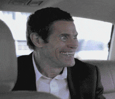 Celebrity gif. Willem DaFoe sitting in a car, with confused eyes and a huge, unnerving grin.