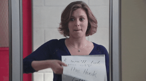 TV gif. Rachel Bloom as Rebecca Bunch on Crazy Ex-Girlfriend stands outside of a doorway, holding a notebook. She presses her lips together to hold in a laugh as she turns the page in the notebook to a page that says, “Get it Gurl.”