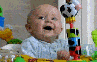 Video gif. Baby sits in a play seat and laughs but then quickly appears startled, jumping and wide-eyed.
